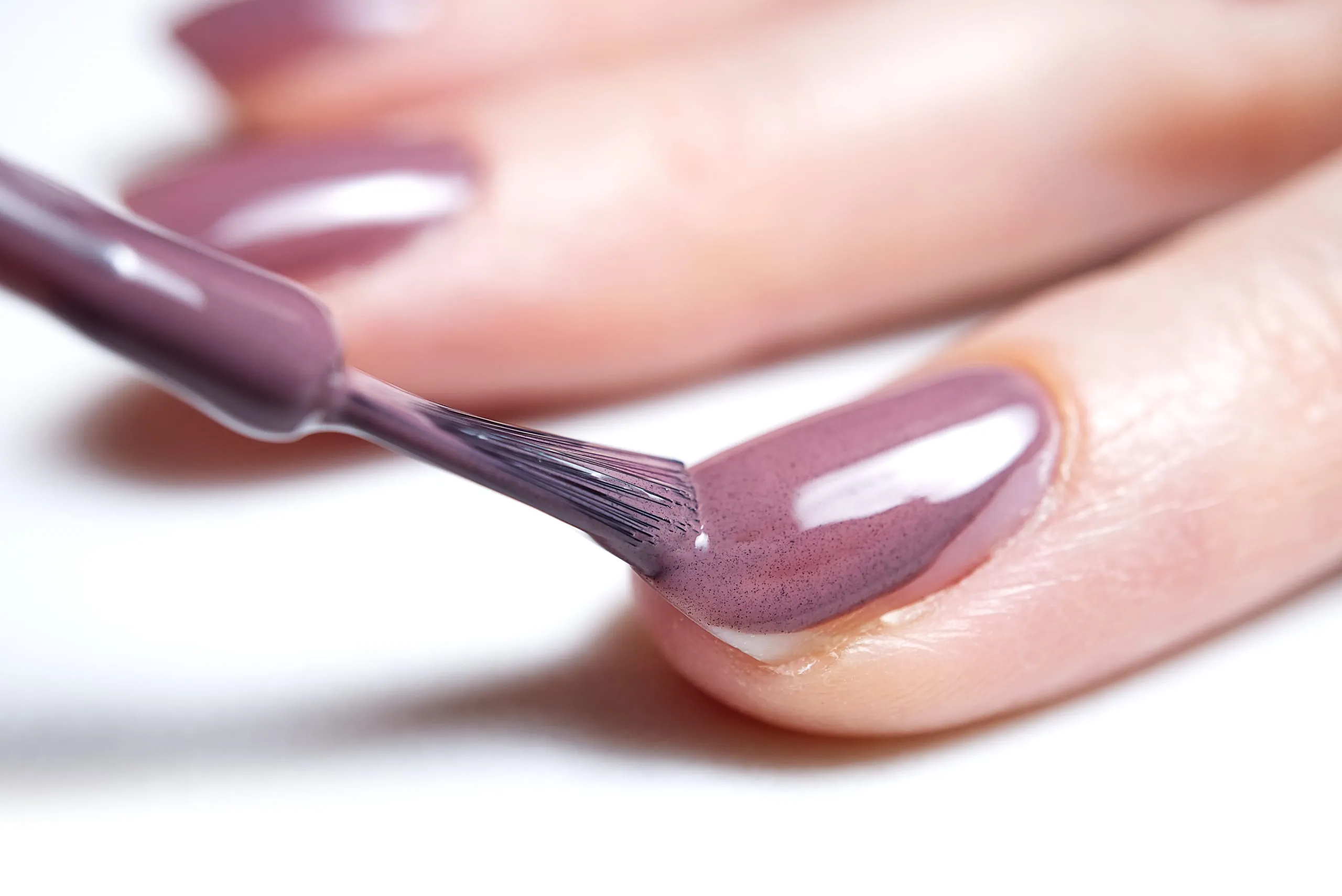 Pinceau appliquant un vernis mauve brillant sur un ongle en gros plan.