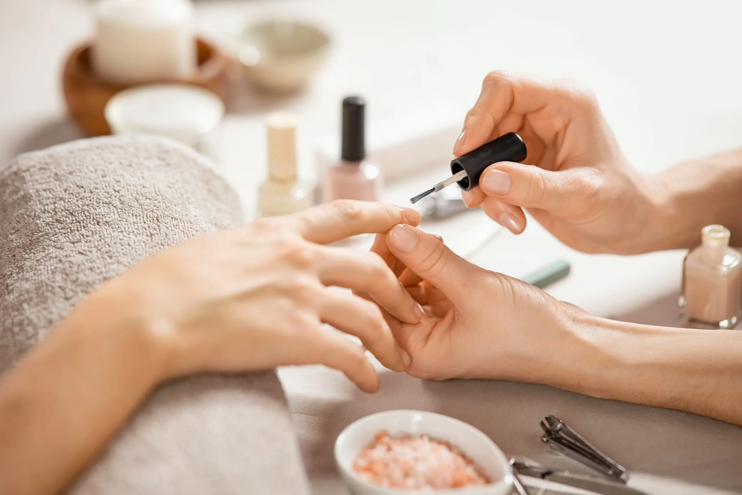Application d'un vernis nude sur les ongles d'une cliente dans un espace de manucure.