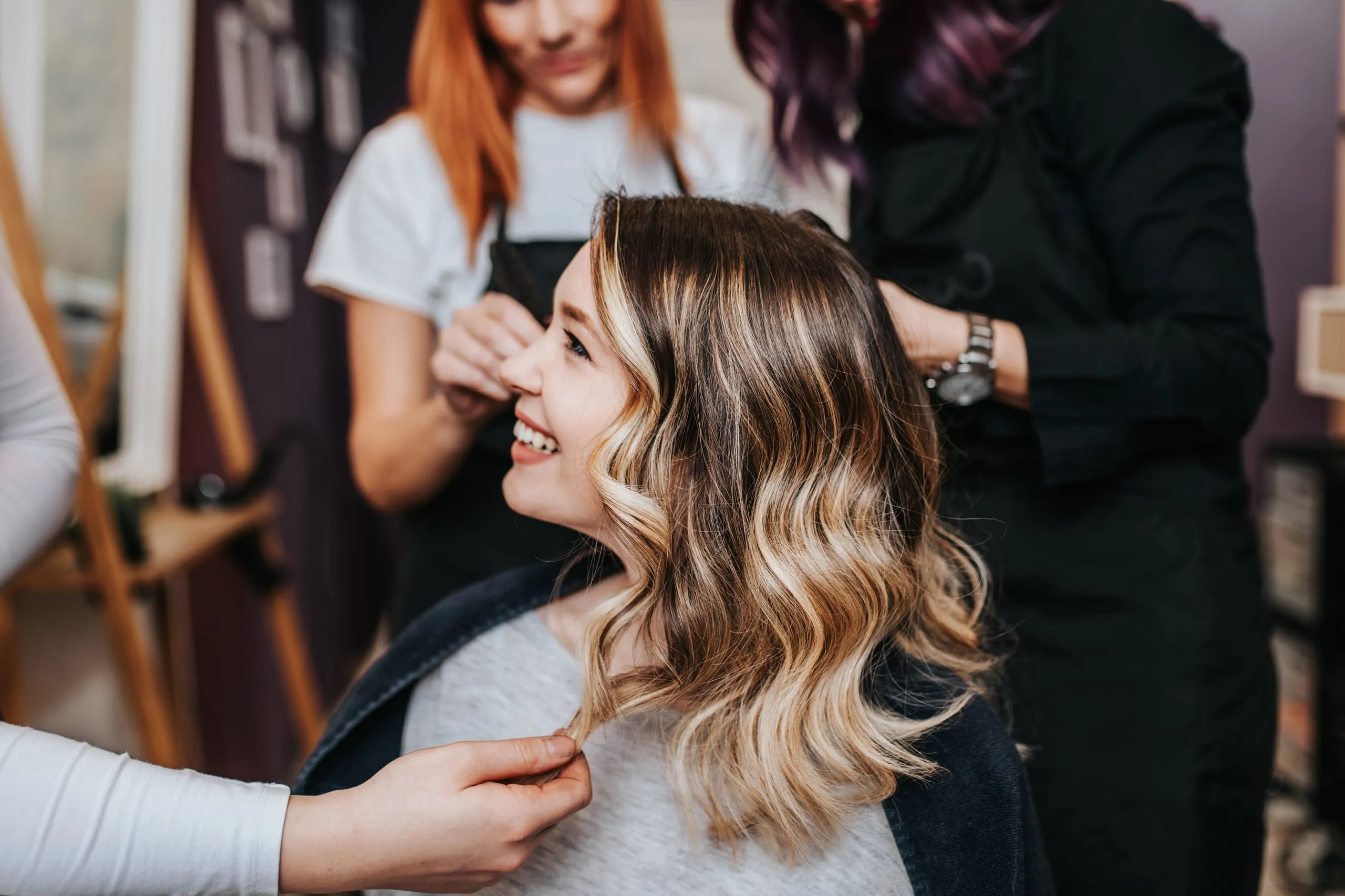 Cliente aux cheveux longs ondulés avec un balayage blond mise en forme par des coiffeuses.