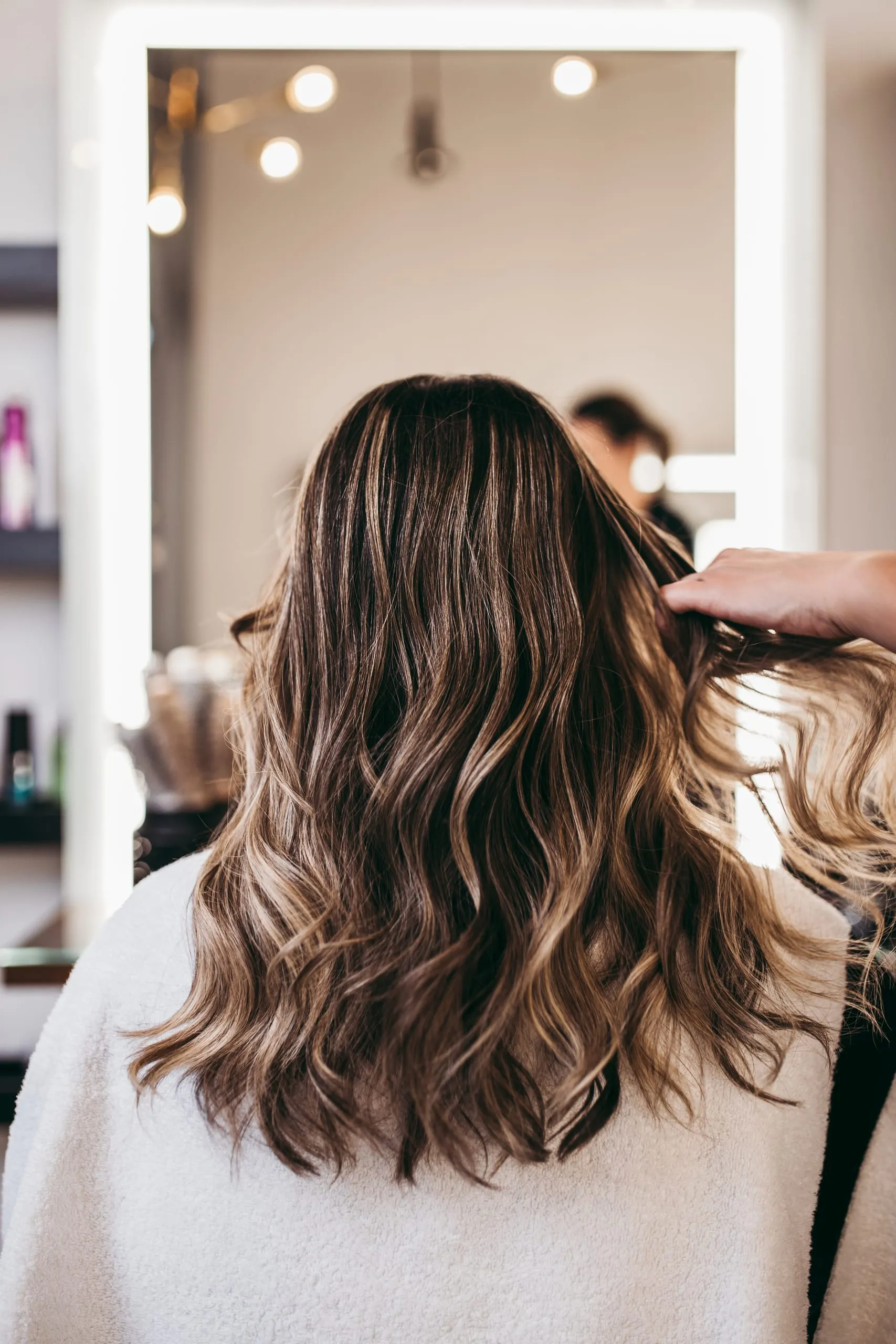 Cheveux mi-longs ondulés avec balayage brun et reflets blonds dans un salon de coiffure.