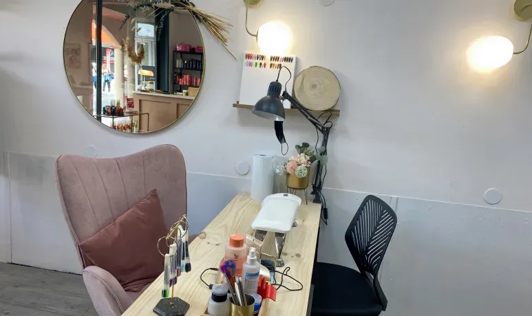 Espace manucure du salon avec table en bois, fauteuil rose et matériel pour les ongles.