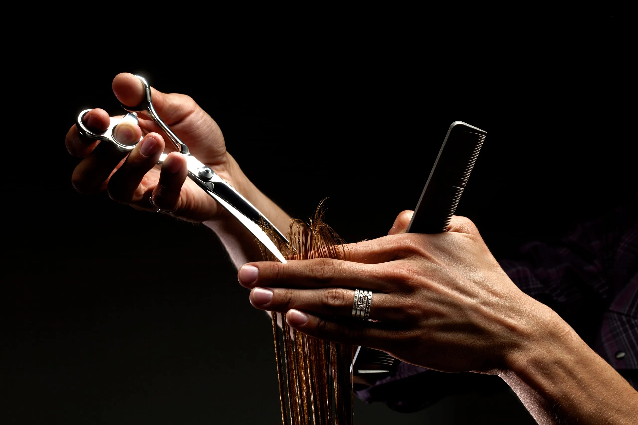 Mains d'une coiffeuse coupant une mèche de cheveux longs et humides avec des ciseaux et un peigne.