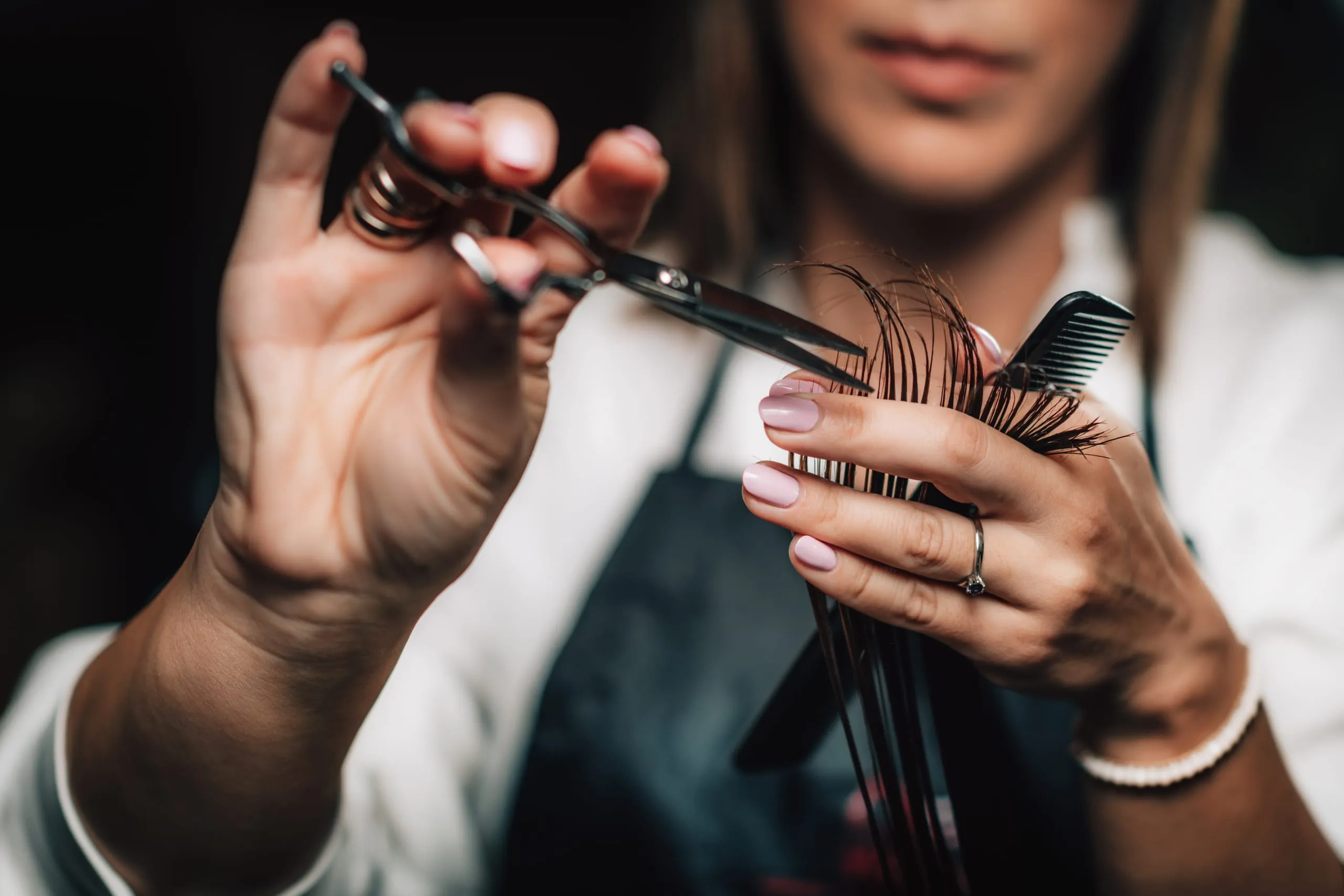 Coiffeuse coupant une mèche de cheveux aux ciseaux avec un peigne.