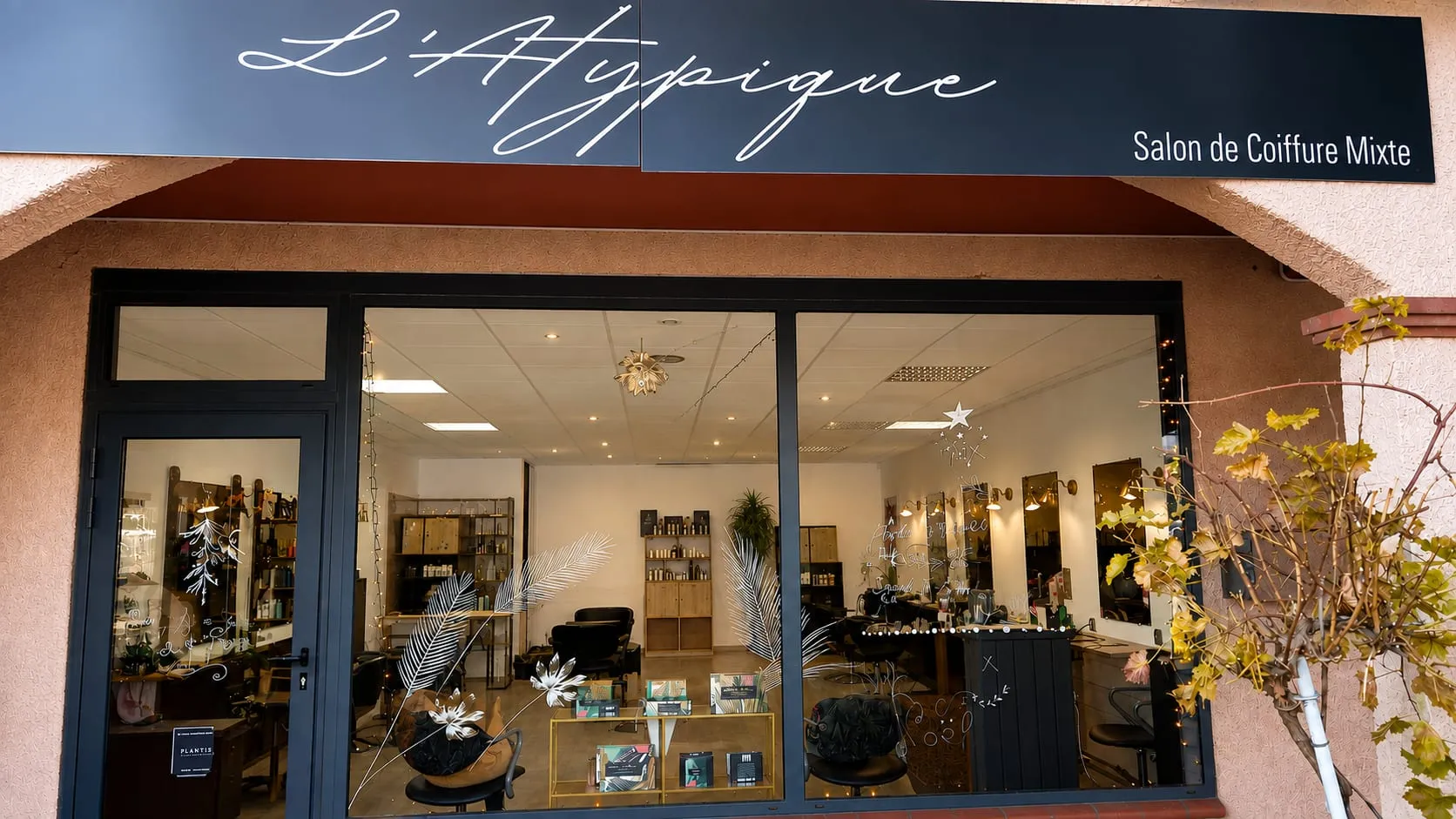 Devanture vitrée du Salon L'Atypique avec son enseigne et les postes de coiffage visibles.