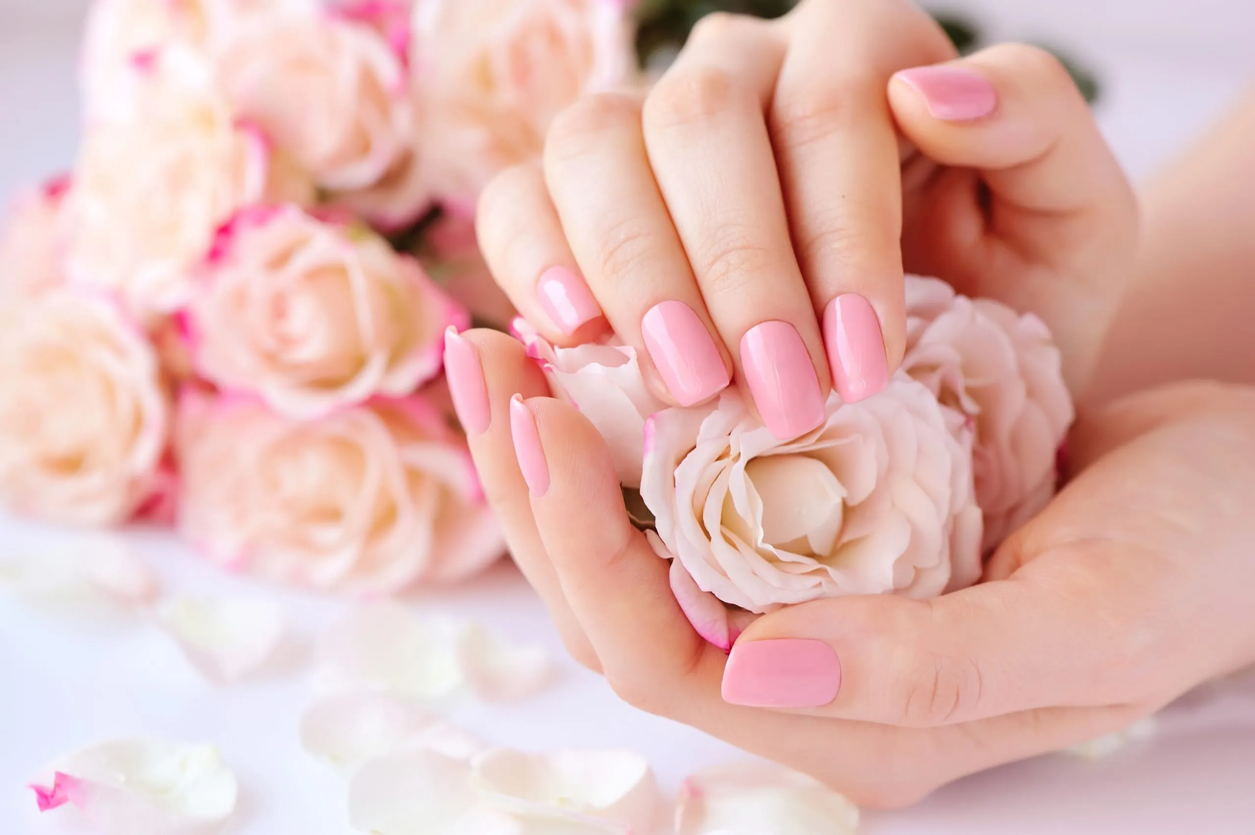 Mains aux ongles rose pastel tenant des fleurs roses et blanches.