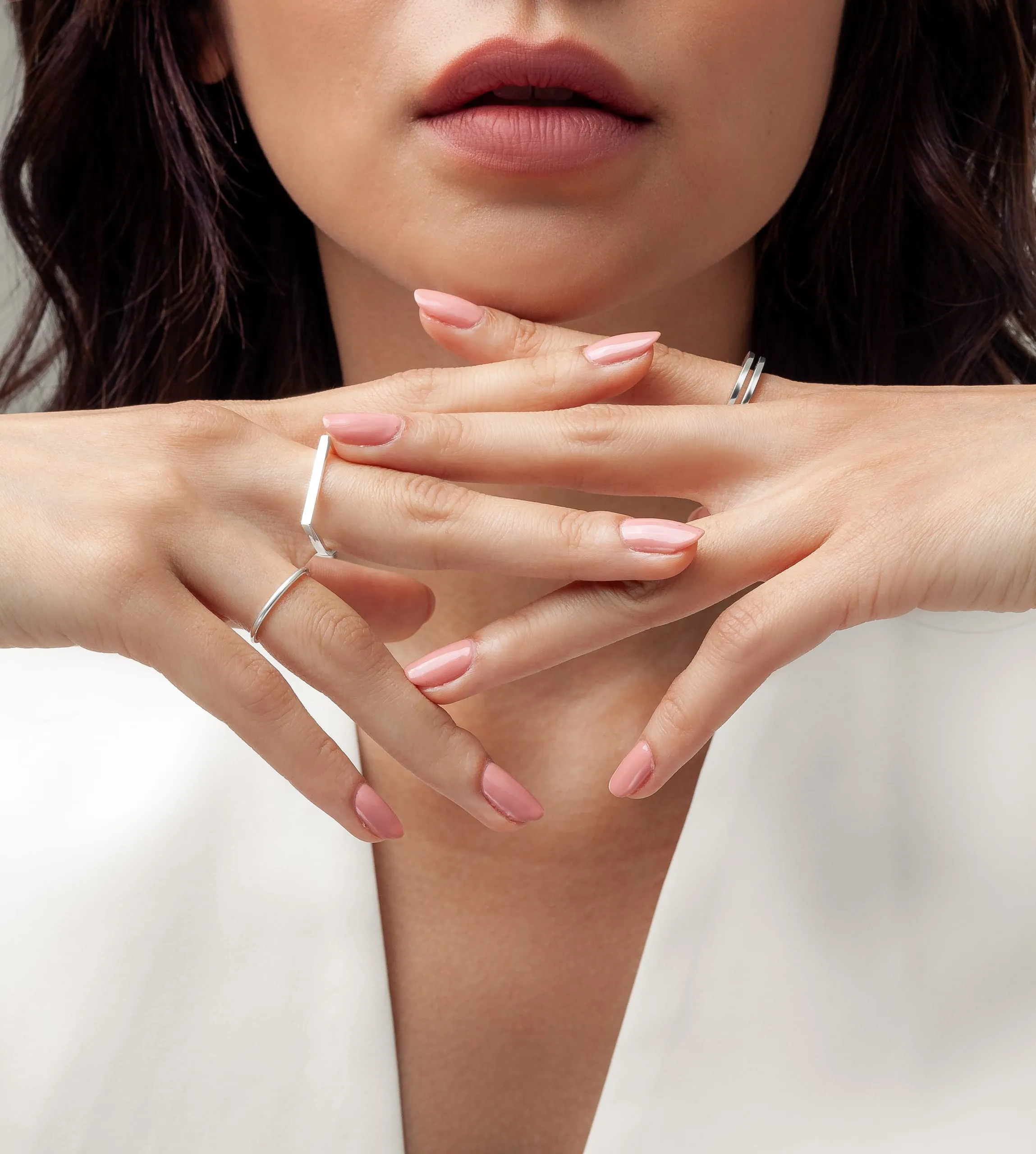 Femme présentant ses ongles rose poudré, les mains croisées devant son visage.