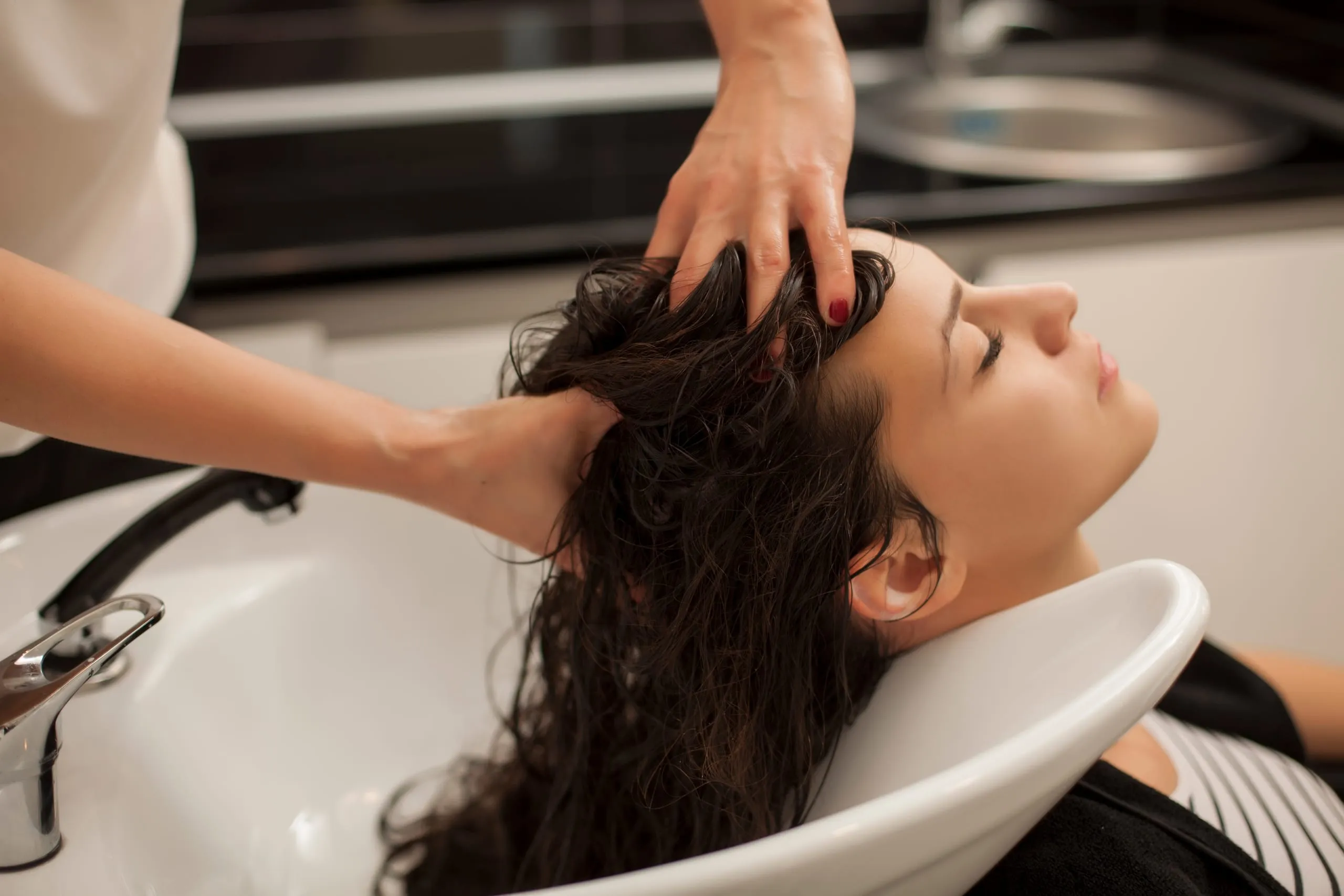 Massage du cuir chevelu d'une cliente installée au bac de lavage.