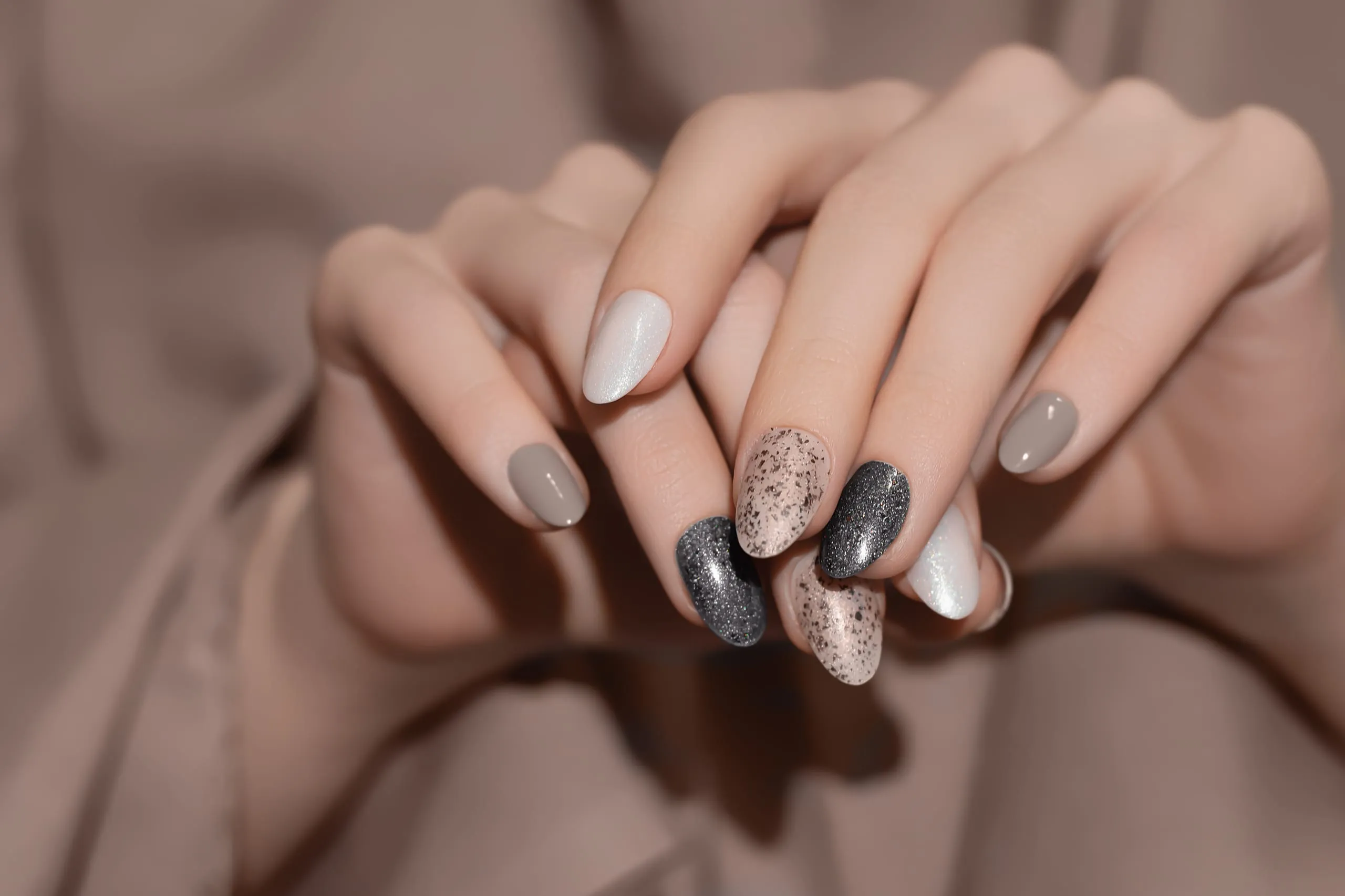 Manucure en amande aux teintes noire, taupe, blanche et pailletée.