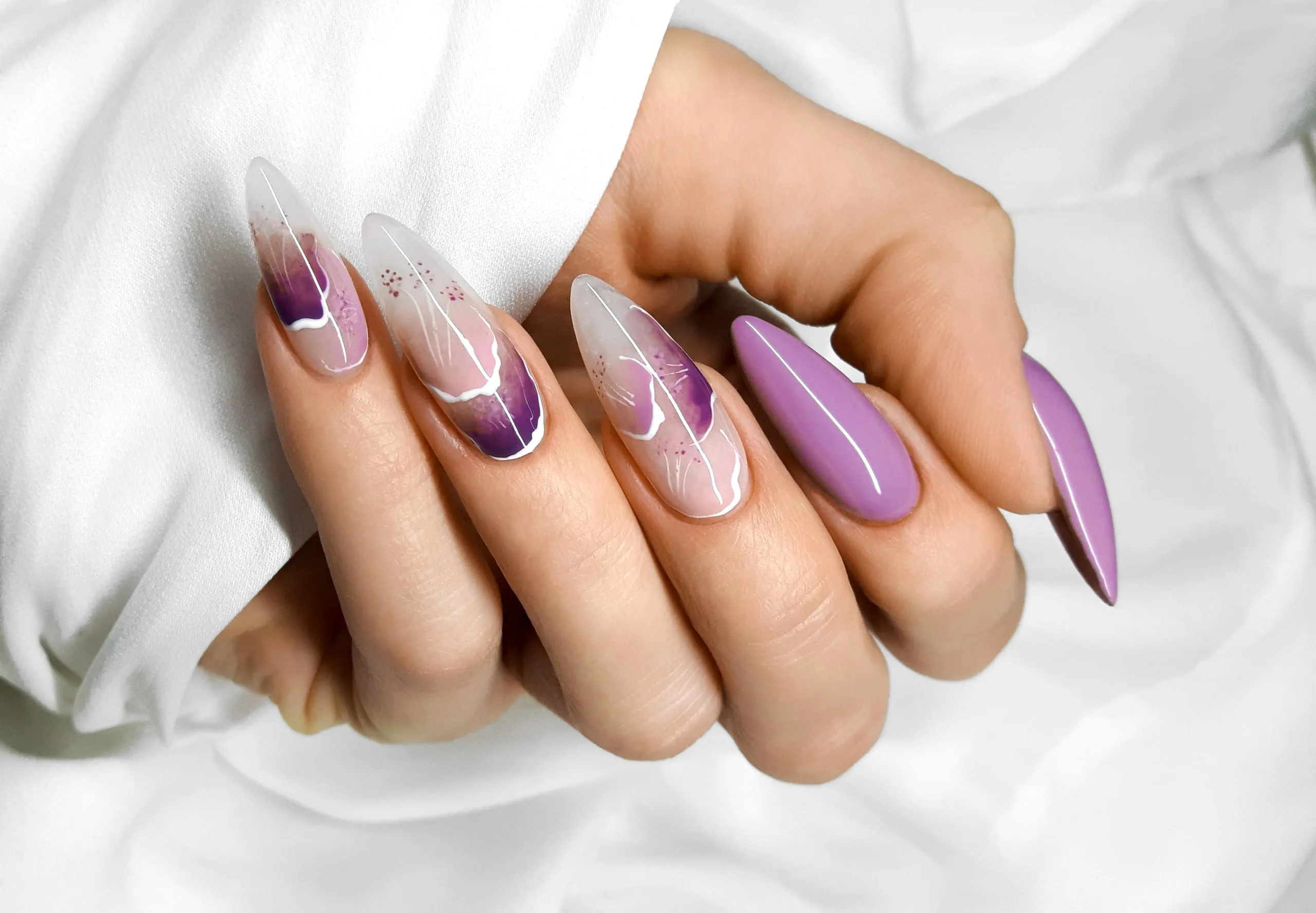 Manucure violette, blanche et rose avec motifs abstraits sur des ongles longs en amande.
