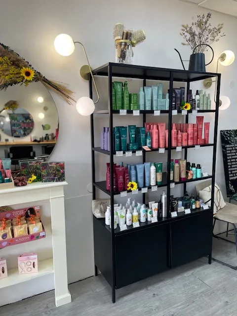 Étagère noire garnie de produits capillaires colorés, entourée de luminaires et de fleurs séchées.