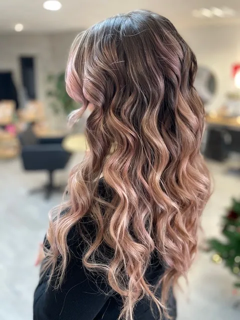 Cheveux longs coiffés en ondulations avec des reflets rose poudré.