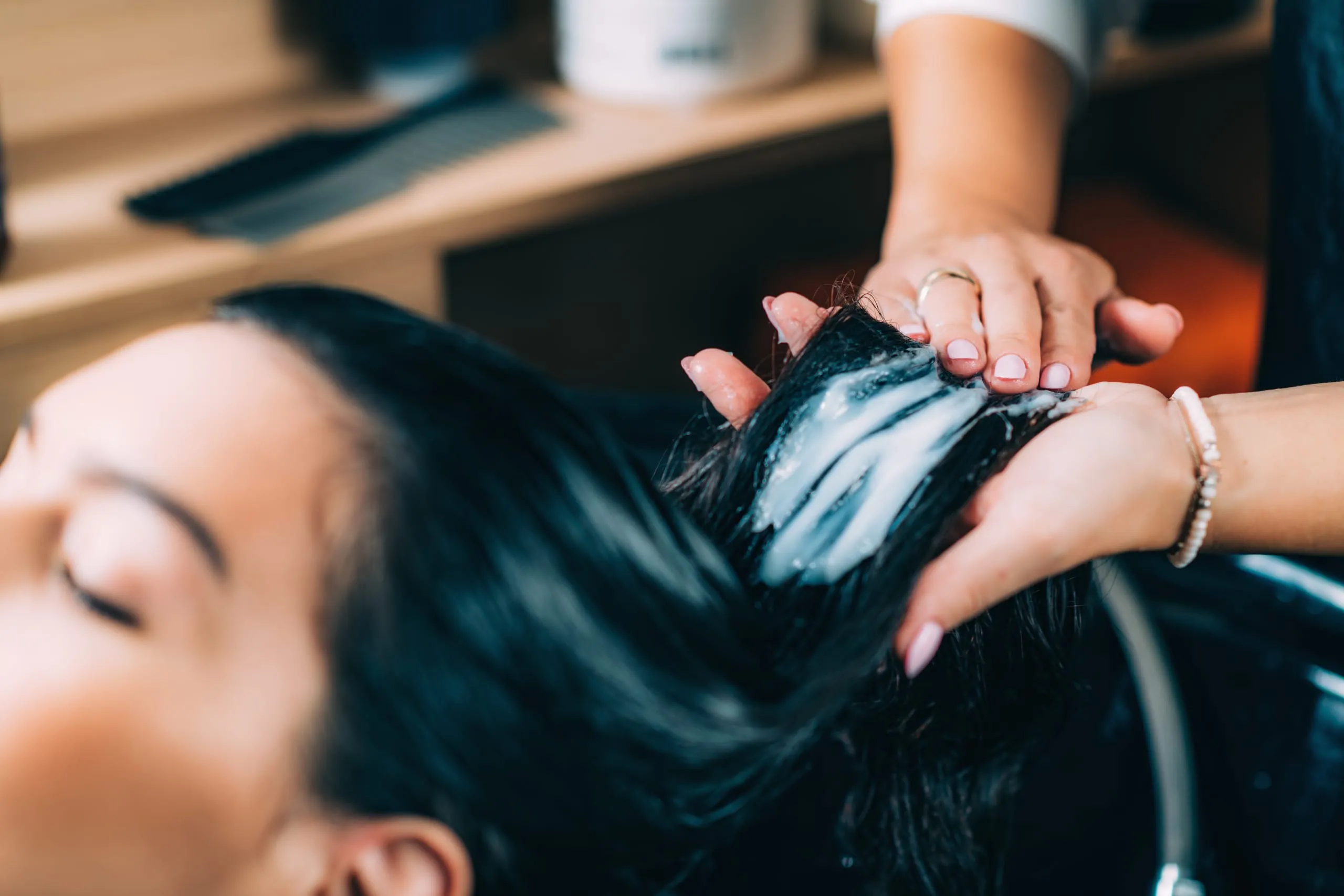Soin capillaire appliqué sur les cheveux d'une cliente installée au bac.