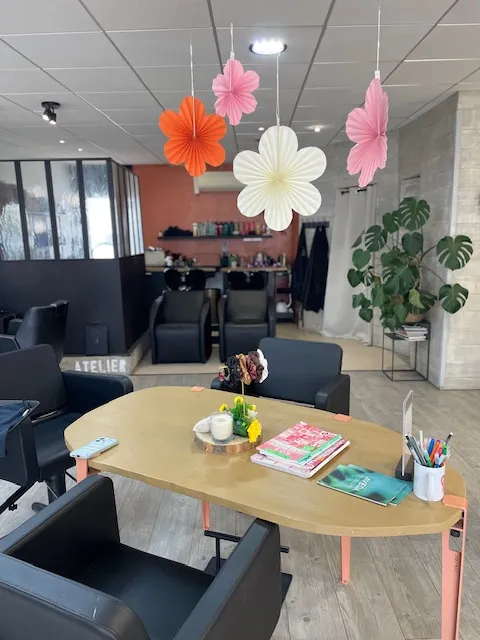 Vue intérieure du salon avec une grande table en bois, des fauteuils noirs et des fleurs suspendues.